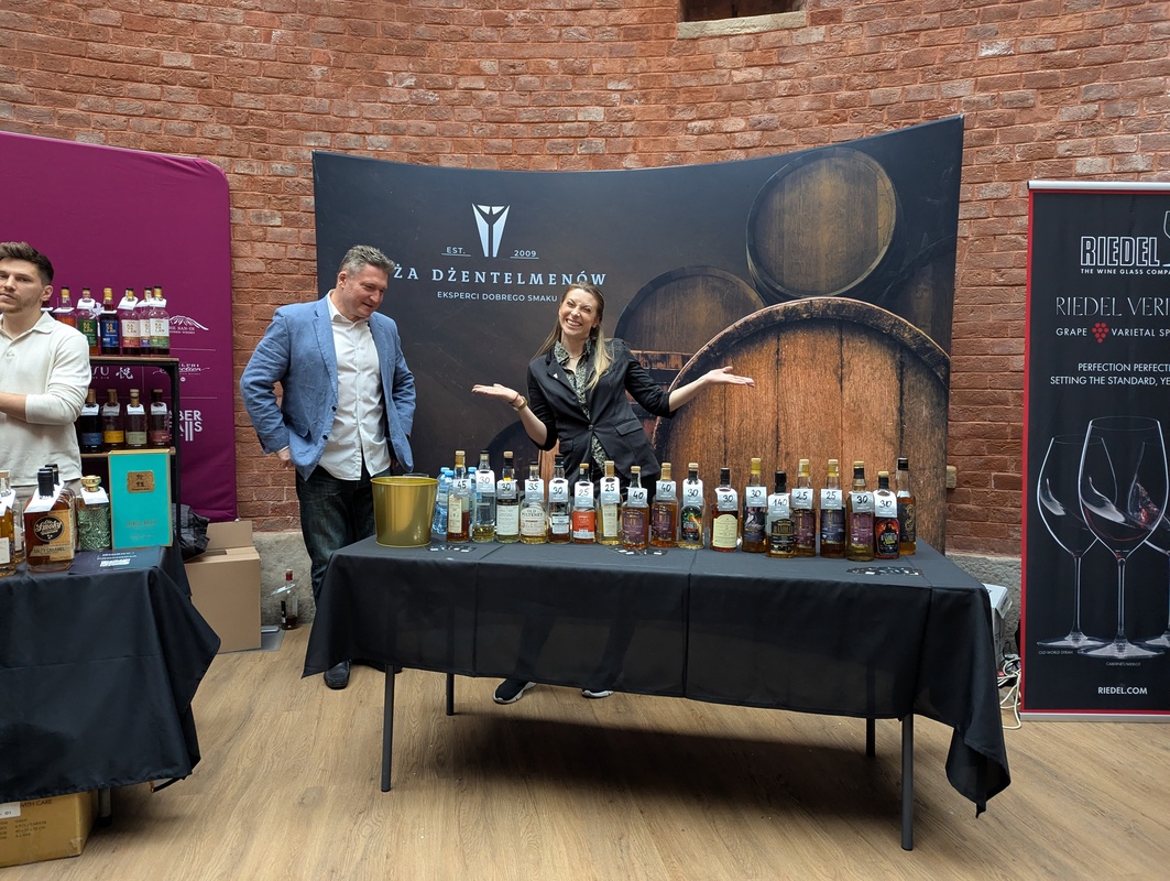 Stoisko Loża Dżentelmenów – miejsce spotkań i degustacji na zdjęciu widoczne jest stoisko loża dżentelmenów, przy którym uczestnicy festiwalu degustują różne trunki podczas whisky day cracow 2025, a na pierwszym planie uśmiechnięta reprezentantka loży dżentelmenów